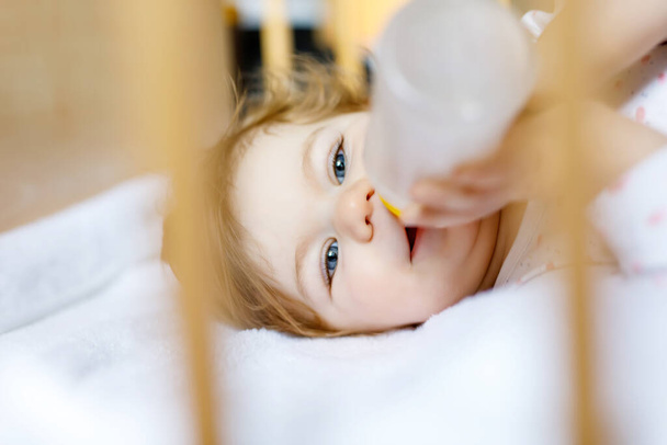 Söpö pikkutyttö, jolla on pullo, jossa on kaava mieto ja juominen. Lapsi vauvansängyssä ennen nukkumista - Valokuva, kuva