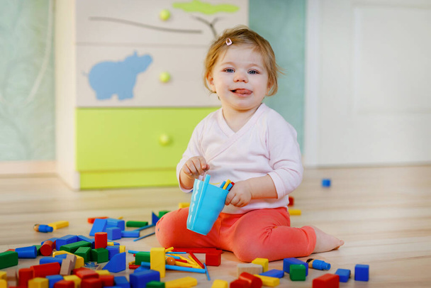 Мила маленька дівчинка грає з освітніми іграшками. Щаслива здорова дитина розважається з різними дерев'яними блоками вдома або в дитячій кімнаті. Повзання дитини і вивчення кольорів і форм, в приміщенні
 - Фото, зображення