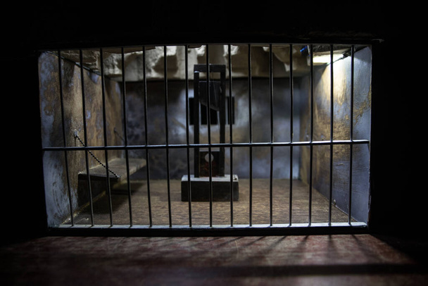 Concetto di esecuzione. Pena di morte ghigliottina in miniatura all'interno della vecchia prigione. Vecchia cella delle sbarre della prigione. Decorazione artistica creativa. Vista dell'orrore del modello in scala di ghigliottina al buio - Foto, immagini