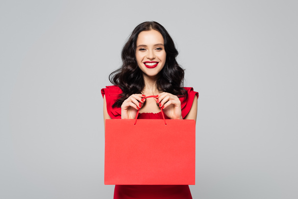 glückliche junge Frau mit Einkaufstasche isoliert auf grau - Foto, Bild