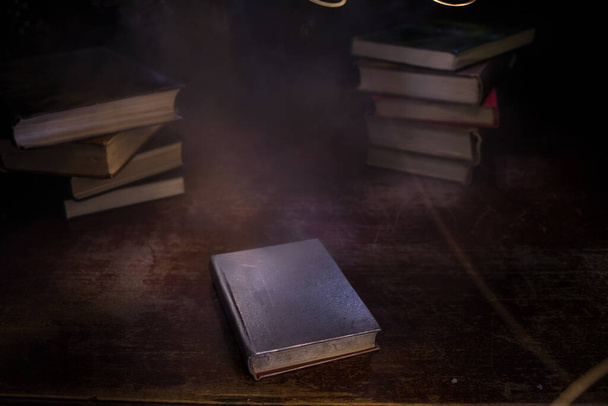 Una pila di vecchi libri. Libro d'epoca su tavolo in legno. Fulmini magici intorno a un libro luminoso nella stanza delle tenebre. Focus selettivo - Foto, immagini