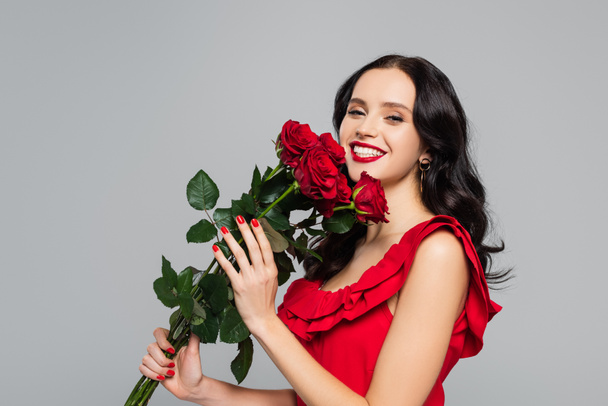 vidám fiatal nő kezében vörös rózsa és mosolygós elszigetelt szürke - Fotó, kép