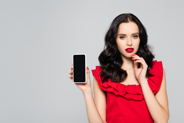 woman with red lips holding smartphone with blank screen isolated on grey - Фото, изображение