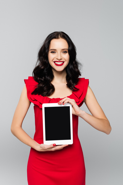 erfreut Frau mit roten Lippen hält digitale Tablette mit leerem Bildschirm isoliert auf grau - Foto, Bild