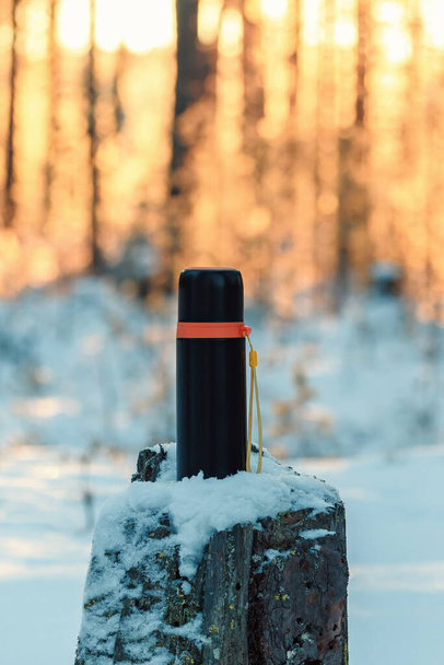 Thermos sur souche de pin dans la forêt d'hiver. Randonnée hivernale et concept de loisirs - Photo, image