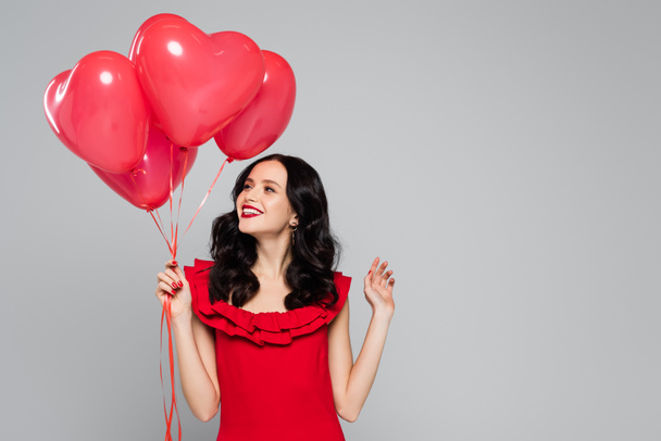 happy woman holding red heart-shaped balloons isolated on grey - Fotografie, Obrázek