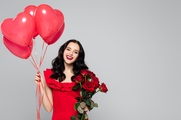happy woman holding red heart-shaped balloons and roses isolated on grey - Photo, Image