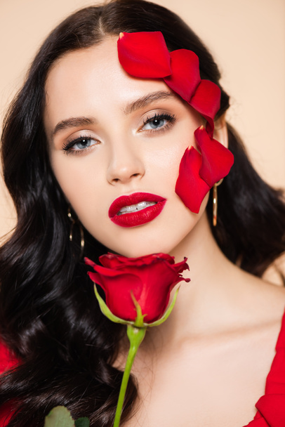 brunette young woman with red lips and petals of rose on face isolated on pink - Φωτογραφία, εικόνα