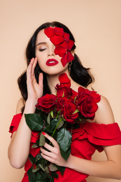 brunette woman with closed eyes and petals on face near roses isolated on pink - 写真・画像