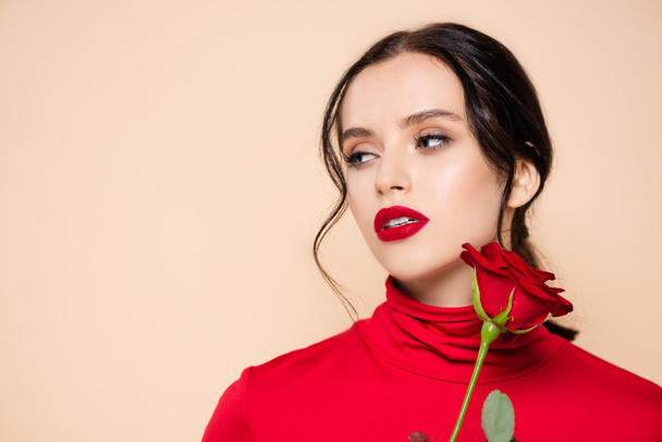 brunette woman with red lips holding red rose and looking away isolated on pink - Photo, Image