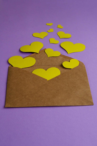 Brown envelope with yellow hearts on lilac background with copy space. Valentine's day concept - Photo, Image