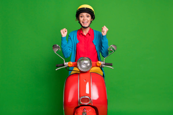 Photo of young cheerful smiling excited good mood girl hold fists in victory ride red moped isolated on green color background - Fotoğraf, Görsel