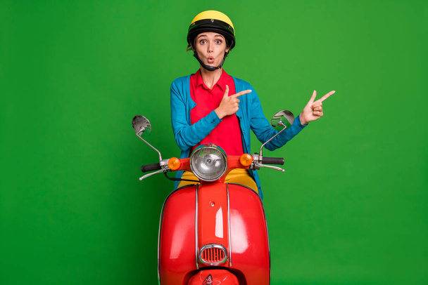 Photo of young attractive shocked amazed girl pointing finger copyspace ride red moped isolated on green color background - Fotoğraf, Görsel