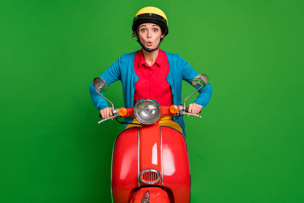 Photo of young beautiful shocked amazed surprised girl wear yellow helmet ride red moped isolated on green color background - Fotoğraf, Görsel