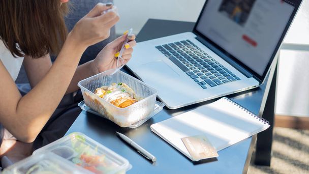 Bilgisayarında yemek yiyen ve çalışan bir kadın evinde ciddi bir şekilde oturuyor ya da sosyal ağlarda arkadaşlarıyla sohbet ediyor.. - Fotoğraf, Görsel