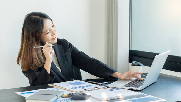 Vista laterale di una donna d'affari asiatica sorridente che lavora da casa e grafico sul tavolo - Foto, immagini