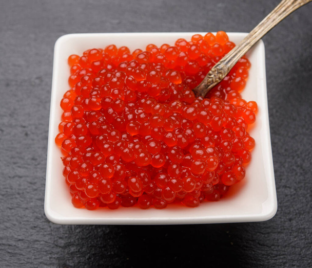 caviar de saumon kéta rouge dans un bol en céramique blanche sur fond de pierre d'ardoise noire, gros plan - Photo, image