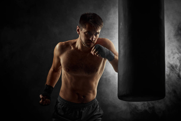 Male boxer punching in boxing bag on black background - Foto, Imagen