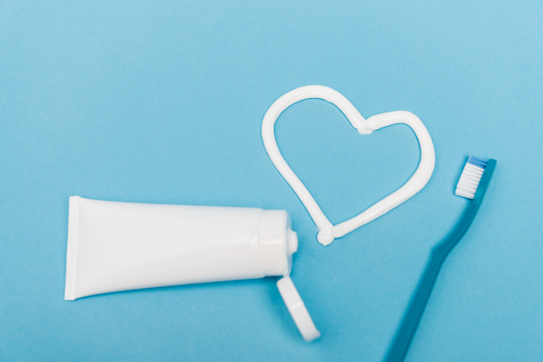 Vista superior del tubo cerca del corazón de pasta de dientes y cepillo de dientes sobre fondo azul - Foto, Imagen