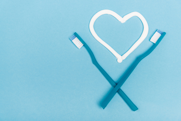 Vue du dessus des brosses à dents près du coeur signe du dentifrice sur fond bleu - Photo, image