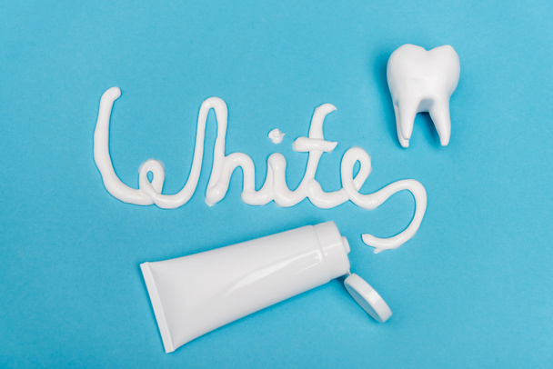 Vista superior de letras blancas cerca del tubo de pasta de dientes y modelo de dientes sobre fondo azul - Foto, imagen