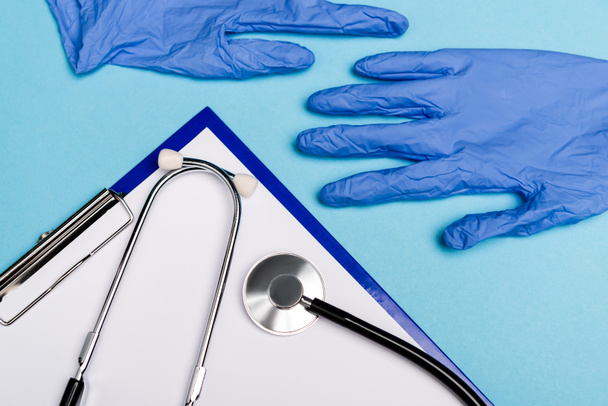 Top view of clipboard, stethoscope and latex gloves on blue background - 写真・画像