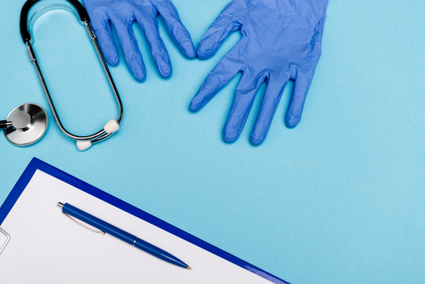 Top näkymä lateksi käsineet lähellä stetoskooppi ja leikepöydälle kynä sinisellä pohjalla - Valokuva, kuva