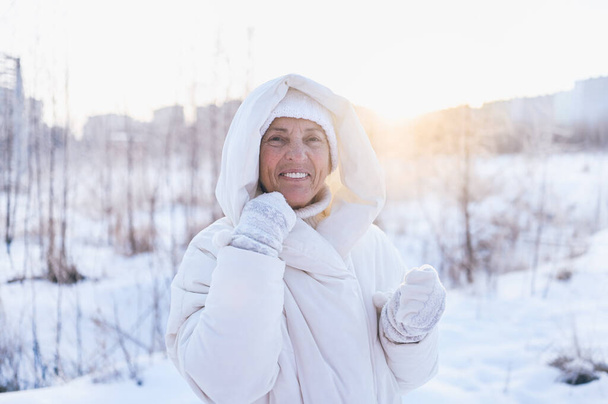 Iloinen vanhempi kypsä nainen valkoisessa lämmin outtwear leikkii lunta aurinkoinen talvi ulkona. Eläkkeellä olevat terveet ihmiset loma talvi toimintaa, aktiivinen elämäntapa käsite - Valokuva, kuva