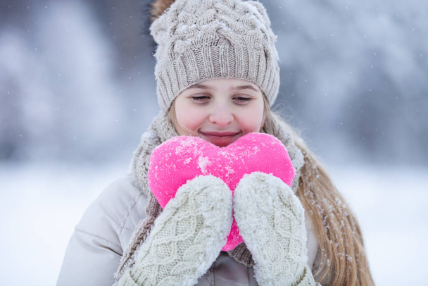 Ritratto di una graziosa ragazza bionda che indossa caldi vestiti a maglia con un cuore rosa su sfondo innevato invernale. Amare l'inverno o il concetto di giorno di S. Valentino. - Foto, immagini