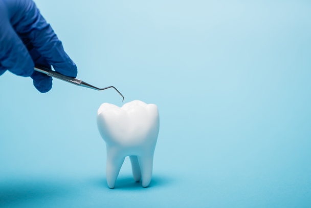 Close up view of dentist holding tool near white model of tooth on blue background - Foto, Imagen