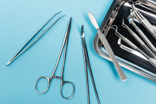 Top view of dental tools near metal tray on blue background - Фото, зображення