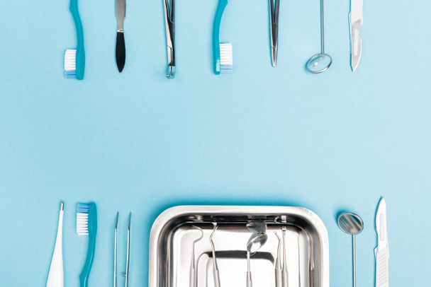 Vista dall'alto di strumenti dentali, vassoio e spazzolini da denti su sfondo blu con spazio per la copia  - Foto, immagini