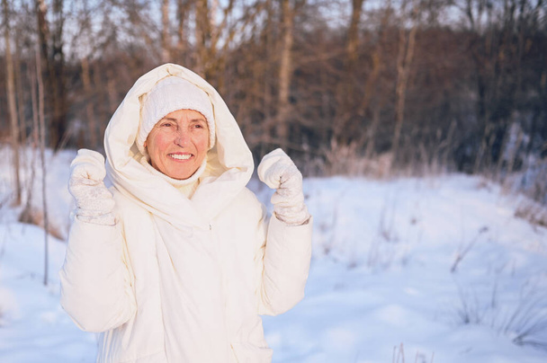 Szczęśliwy starszy starszy kobieta w białej ciepłej bieliźnie bawiąc się śniegiem w słonecznej zimie na świeżym powietrzu. Emeryci zdrowi ludzie wakacje wakacje zimowe zajęcia, koncepcja aktywnego stylu życia - Zdjęcie, obraz