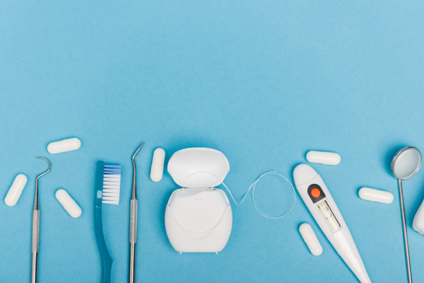 Κάτοψη οδοντιατρικών εργαλείων, χαπιών και θερμόμετρου σε μπλε φόντο - Φωτογραφία, εικόνα