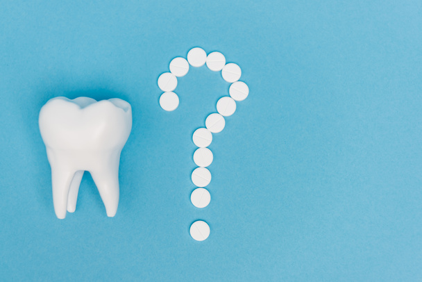 Top view of tooth model and question mark from pills on blue background - Фото, изображение
