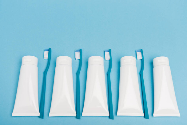 Top view of blue toothbrushes and white tubes of toothpaste on blue background - Foto, afbeelding