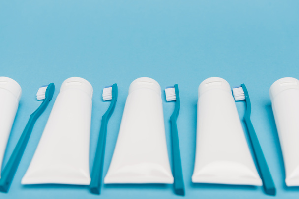 White tubes with toothpaste and toothbrushes on blurred foreground on blue background - Foto, afbeelding