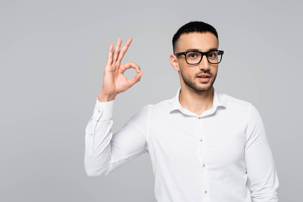 young hispanic manager in eyeglasses showing ok gesture isolated on grey - Photo, Image