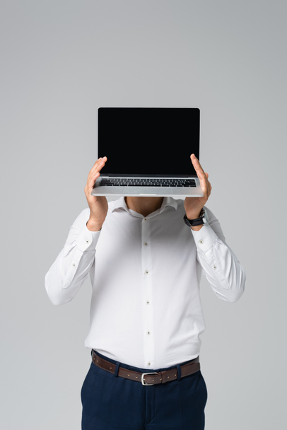 Latynoski menedżer w białej koszuli zasłania twarz z laptopem odizolowanym na szaro - Zdjęcie, obraz
