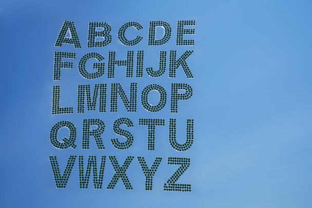 Set - the English alphabet from green rhinestones on blue sky background. ABC - Zdjęcie, obraz