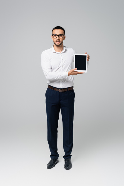 full length view of hispanic businessman showing digital tablet with blank screen on grey - Zdjęcie, obraz