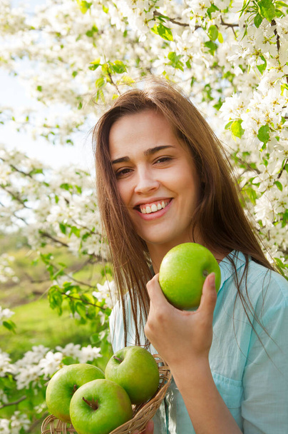 Portrait of face young latin hispanic woman holding apple on Spring blooming apple tree background. summer nature. spring time season.Pretty in establishment of branches of a blossoming apple - Valokuva, kuva
