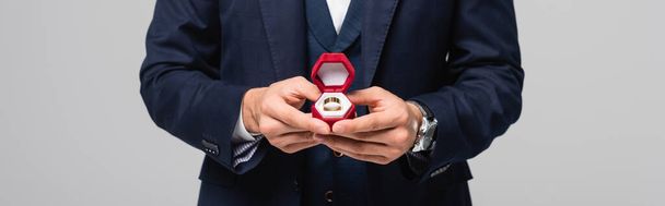 partial view of man in suit holding jewelry box with wedding ring isolated on grey, banner - Photo, Image