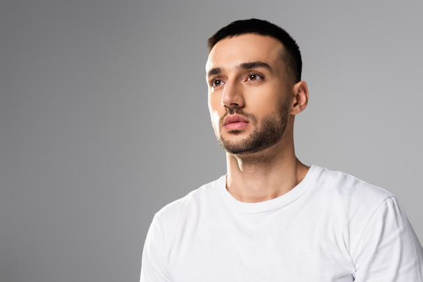 zelfverzekerd, brunette hispanic man in wit t-shirt weg kijkend geïsoleerd op grijs - Foto, afbeelding