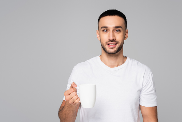 smiling hispanic man in t-shirt holding white cup isolated on grey - Fotografie, Obrázek