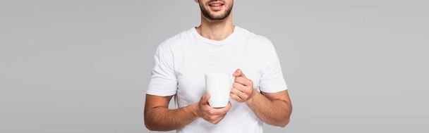 partial view of smiling man in white t-shirt holding cup isolated on grey, banner - 写真・画像