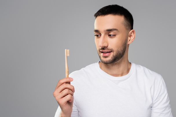 молодий, бородатий чоловік тримає зубну щітку ізольовано на сірому
 - Фото, зображення