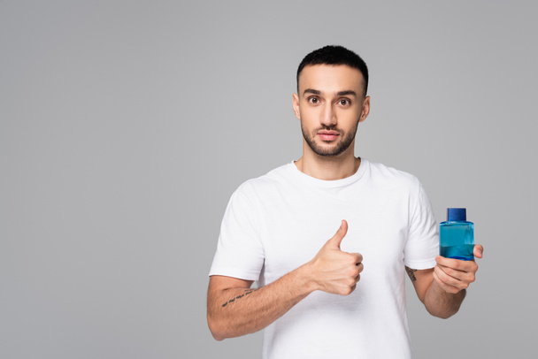brunette hispanic man showing thumb up while holding toilette water isolated on grey - Fotoğraf, Görsel