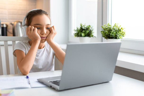 Primer plano foto anuncio niña alumno en los auriculares delante de un monitor de ordenador portátil durante una lección en línea. - Foto, imagen