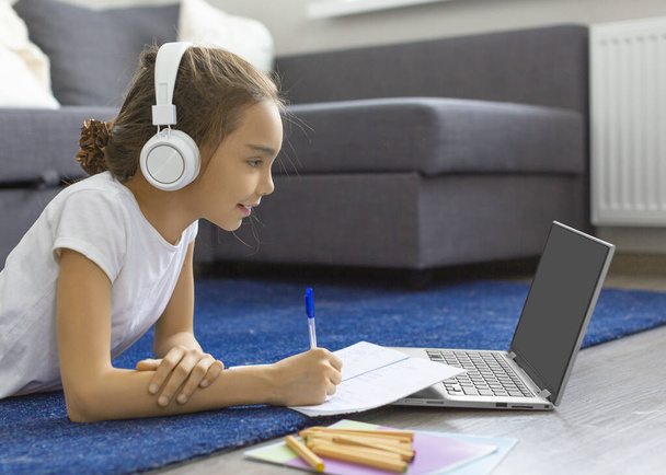 Teenager-Mädchen macht ihre Hausaufgaben online vor einem Laptop-Monitor, der zu Hause auf dem Boden liegt. - Foto, Bild